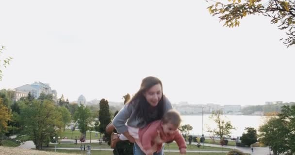 Mujer joven y bonita sosteniendo a la niña en sus brazos al atardecer en el parque. Feliz madre jugando, abrazando y besando a su pequeña hija — Vídeo de stock