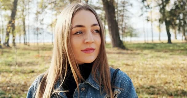 Retrato de jovem fêmea atraente que sorrindo e olhando para a câmera no parque de outono. Mulher alegremente bonita com o tempo ensolarado. Fechar — Vídeo de Stock