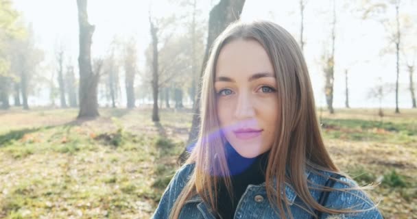 Retrato de jovem fêmea atraente olhando para a câmera deslizante no parque de outono. Mulher alegremente bonita com o tempo ensolarado. Fechar — Vídeo de Stock