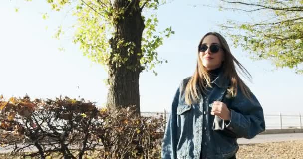 Jong vrolijk lachend meisje wandelend in het herfstpark. Jonge aantrekkelijke vrouw loopt en glimlacht in de zonnestralen — Stockvideo