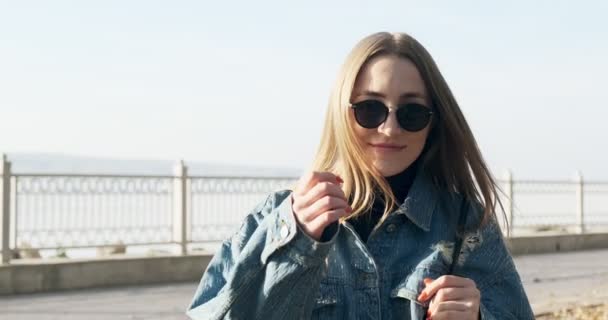 Młoda uśmiechnięta dziewczyna spacerująca po jesiennym parku. Młoda atrakcyjna kobieta spaceruje i uśmiecha się w promieniach słońca — Wideo stockowe