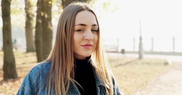 Portrait of young attractive female who smiling and looking at the camera on autumn park. Cheerfully pretty woman at sunny weather. Close up — ストック動画