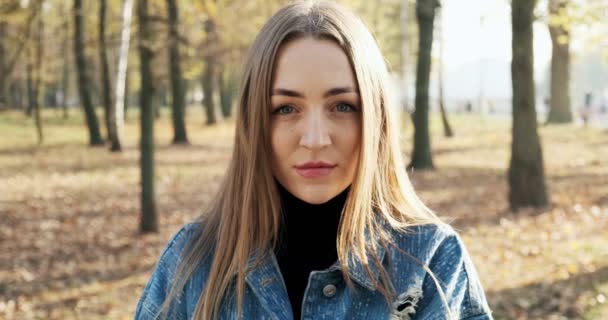 Portret van een jonge aantrekkelijke vrouw die glimlacht en naar de camera kijkt in het herfstpark. Vrolijk mooie vrouw bij zonnig weer. Sluiten. — Stockvideo