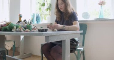 Kadın oyuncak bebek seramik parçası yapıyor. Kadın evde oturuyor ve masada bebek için kulak yapıyor. Çömlek bebekleri parçaları, el yapımı ve yaratıcı yetenekler