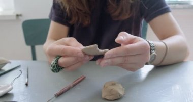 Kadın oyuncak bebek seramik parçası yapıyor. Kadın evde oturuyor ve masada bebek için kulak yapıyor. Çömlek bebekleri parçaları, el yapımı ve yaratıcı yetenekler