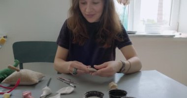 Kadın oyuncak bebek seramik parçası yapıyor. Kadın evde oturuyor ve masada bebek için kulak yapıyor. Çömlek bebekleri parçaları, el yapımı ve yaratıcı yetenekler