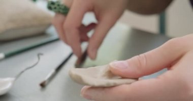 Kadın oyuncak bebek seramiği yapıyor. Kadın evde oturuyor ve masada bebek için kulak yapıyor. Çömlek bebekleri parçaları, el yapımı ve yaratıcı yetenekler