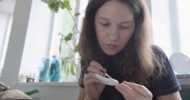 Kadın oyuncak bebek seramik parçası yapıyor. Kadın evde oturuyor ve masada bebek için kulak yapıyor. Çömlek bebekleri parçaları, el yapımı ve yaratıcı yetenekler