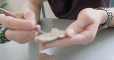 Kadın oyuncak bebek seramiği yapıyor. Kadın evde oturuyor ve masada bebek için kulak yapıyor. Çömlek bebekleri parçaları, el yapımı ve yaratıcı yetenekler