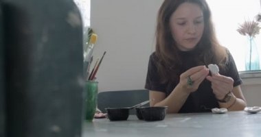 Kadın oyuncak bebek seramik parçası yapıyor. Kadın evde oturuyor ve masada bebek için kulak yapıyor. Çömlek bebekleri parçaları, el yapımı ve yaratıcı yetenekler