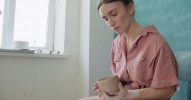 Dişi çömlekçi oturuyor ve bir fincan yapıyor. Kadın seramik bir şey yapıyor. Çömlekçilik, el yapımı ve yaratıcı beceriler