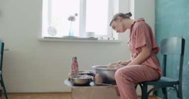 Kadın çömlekçi oturuyor ve çömlek çarkında bir fincan yapıyor. Kadın seramik bir şey yapıyor. Çömlekçilik, el yapımı ve yaratıcı beceriler