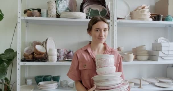 Retrato de una joven sonriente y atractiva alfarera permaneciendo y sosteniendo tazones de barro. Mujer haciendo artículo de cerámica. Trabajo de cerámica, habilidades hechas a mano y creativas — Vídeo de stock