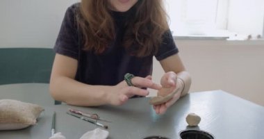 Kadın oyuncak bebek seramik parçası yapıyor. Kadın evde oturuyor ve masada bebek için kulak yapıyor. Çömlek bebekleri parçaları, el yapımı ve yaratıcı yetenekler