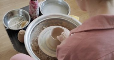 Kadın çömlekçi oturuyor ve çömlek çarkında bir fincan yapıyor. Kadın seramik bir şey yapıyor. Çömlekçilik, el yapımı ve yaratıcı beceriler