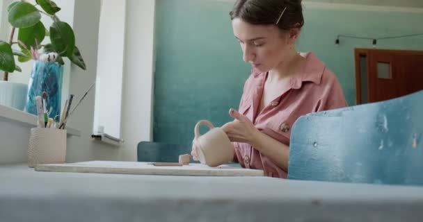 Žena hrnčíř sedí a dělá šálek u stolu. Žena vyrábějící keramické předměty. Pottery working, handmade and creative skills — Stock video