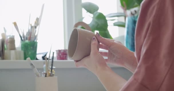 Ceramista donna seduta e fa una tazza a tavola. Donna che fa oggetti in ceramica. Lavorazione della ceramica, abilità artigianali e creative — Video Stock