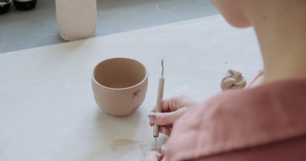 Ceramista donna seduta e fa una tazza a tavola. Donna che fa oggetti in ceramica. Lavorazione della ceramica, abilità artigianali e creative — Video Stock