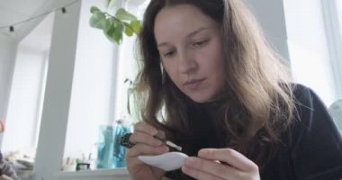 Kadın oyuncak bebek seramik parçası yapıyor. Kadın evde oturuyor ve masada bebek için kulak yapıyor. Çömlek bebekleri parçaları, el yapımı ve yaratıcı yetenekler