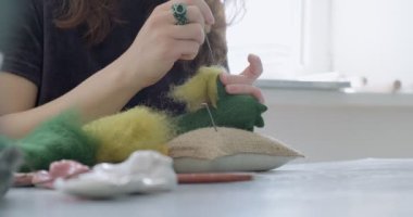Masada yün oyuncak bebek yapan bir kadın var. Kadın evde oturup meşe bebek yapıyor. İğne Keçeli El yapımı ve yaratıcı yetenekler