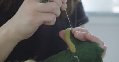Masada yün oyuncak bebek yapan bir kadın var. Kadın evde oturup meşe bebek yapıyor. İğne Keçeli El yapımı ve yaratıcı yetenekler