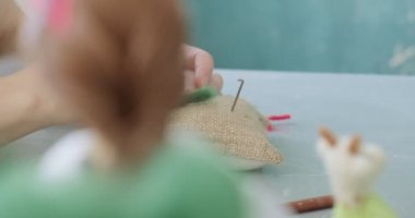 Masada yün oyuncak bebek yapan bir kadın var. Kadın evde oturup meşe bebek yapıyor. İğne Keçeli El yapımı ve yaratıcı yetenekler