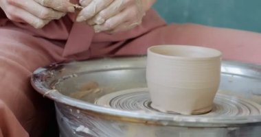 Kadın çömlekçi oturuyor ve çömlek çarkında bir fincan yapıyor. Kadın seramik bir şey yapıyor. Çömlekçilik, el yapımı ve yaratıcı beceriler