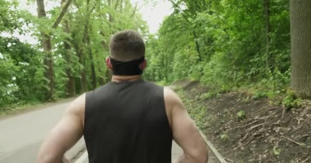 Homem jovem com máscara facial em Sportswear Correndo na estrada na floresta. Homens fazendo exercício de corrida intensa — Vídeo de Stock