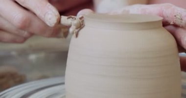 Kadın çömlekçi oturuyor ve çömlek çarkında bir fincan yapıyor. Kadın seramik bir şey yapıyor. Çömlekçilik, el yapımı ve yaratıcı beceriler