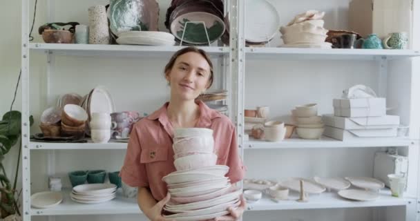 Portret van een jonge glimlachende aantrekkelijke vrouwelijke pottenbakker blijven en houden klei kommen. Een vrouw die keramiek maakt. Pottenbakken, handgemaakte en creatieve vaardigheden — Stockvideo