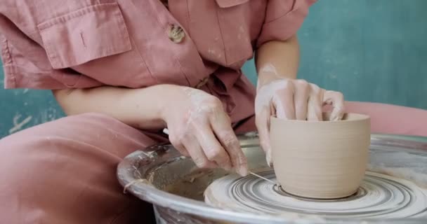 Γυναίκα αγγειοπλάστη κάθεται και κάνει ένα φλιτζάνι στον κεραμικό τροχό. Γυναίκα που φτιάχνει κεραμικά αντικείμενα. Εργασίες αγγειοπλαστικής, χειροποίητες και δημιουργικές δεξιότητες — Αρχείο Βίντεο