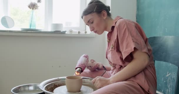 Ceramista femminile seduta e sparare una forma tazza di argilla sulla ruota ceramica. Donna che fa oggetti in ceramica. Cottura della ceramica, abilità artigianali e creative — Video Stock