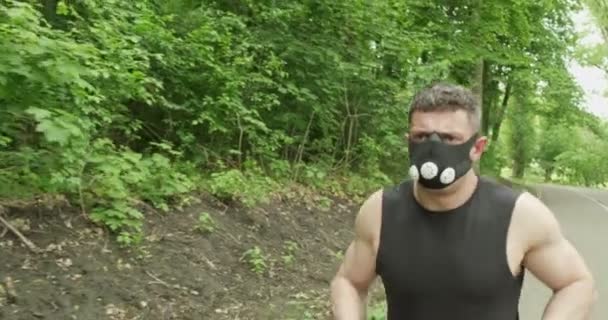 Hombre joven con máscara facial en ropa deportiva corriendo en el camino en el bosque. Hombres haciendo ejercicio de carrera intensa — Vídeo de stock