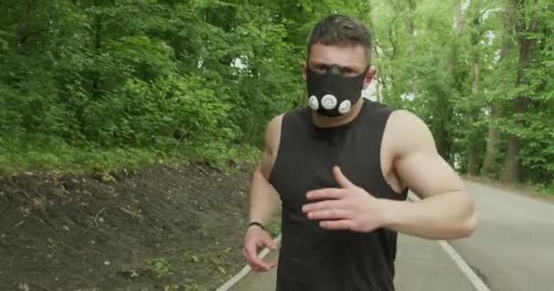 Ung man med ansiktsmask i Sportswear Springa på vägen vid skogen. Män som tränar intensivt — Stockvideo