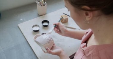 Dişi çömlekçi masada bir fırçayla boya karıştırıyor. Kadın seramik bir şey yapıyor. Çömlekçilik, el yapımı ve yaratıcı beceriler