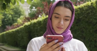 Güzel genç bir kadın akıllı telefona bakıyor, geleneksel türban takıyor. Türbanlı çekici kadın.