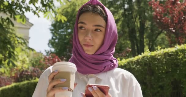 Belle jeune femme boit du café et regarde smartphone, portant un foulard traditionnel. Attrayant femelle dans le hijab — Video