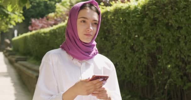 Hermosa mujer joven mirando el teléfono inteligente, usando el pañuelo de cabeza tradicional. Atractiva hembra en hijab — Vídeos de Stock