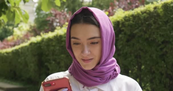 Wanita muda yang cantik melihat smartphone, mengenakan kerudung tradisional. Perempuan Atraktif dalam jilbab — Stok Video