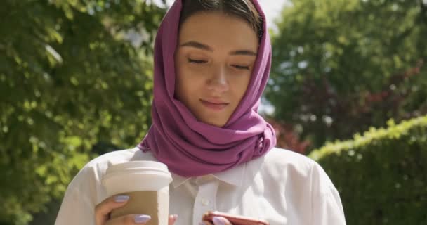 Belle jeune femme boit du café et regarde smartphone, portant un foulard traditionnel. Attrayant femelle dans le hijab — Video