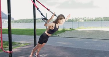Güzel, genç bir kadın spor yapıyor. Açık havada spor kemerleriyle. Çekici bir kadın eğitimi. TRX