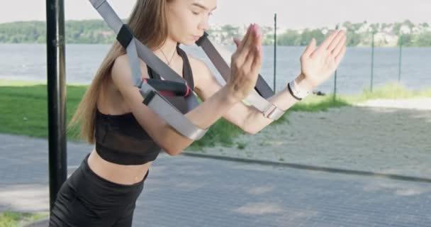 Hermosa mujer joven hace el entrenamiento con correas de fitness al aire libre. Atractivo entrenamiento femenino. TRX — Vídeos de Stock