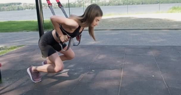 Hermosa mujer joven hace el entrenamiento con correas de fitness al aire libre. Atractivo entrenamiento femenino. TRX — Vídeo de stock