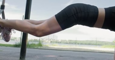 Güzel, genç bir kadın spor yapıyor. Açık havada spor kemerleriyle. Çekici bir kadın eğitimi. TRX