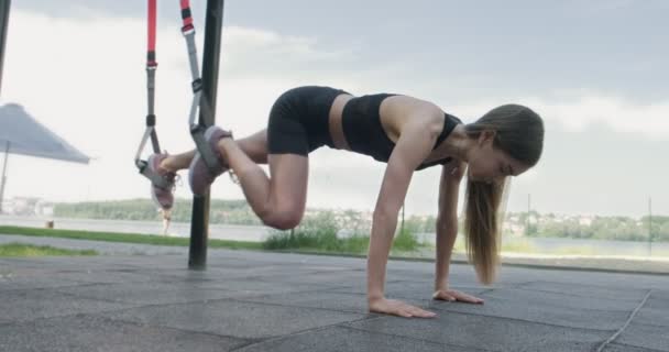 아름다운 젊은 여자는 옥외에서 건강에 좋은 끈으로 훈련을 받는다. 매력적 인 여성 훈련. TRX — 비디오
