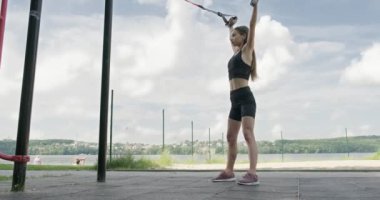 Güzel, genç bir kadın spor yapıyor. Açık havada spor kemerleriyle. Çekici bir kadın eğitimi. TRX
