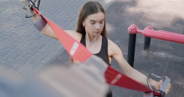 Hermosa mujer joven hace el entrenamiento con correas de fitness al aire libre. Atractivo entrenamiento femenino. TRX — Vídeos de Stock