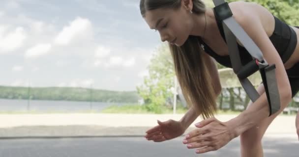 Hermosa mujer joven hace el entrenamiento con correas de fitness al aire libre. Atractivo entrenamiento femenino. TRX — Vídeos de Stock