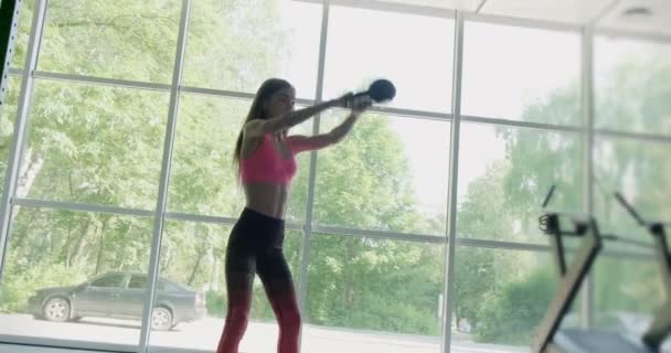 Hermosa joven hace entrenamiento con kettlebell en el gimnasio. Atractivo entrenamiento femenino — Vídeos de Stock