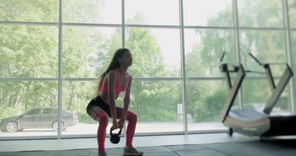 Hermosa joven hace entrenamiento con kettlebell en el gimnasio. Atractivo entrenamiento femenino — Vídeos de Stock